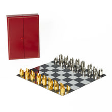 Load image into Gallery viewer, A modern metallic chess set with gold and silver pieces set up on a checkered board next to a closed red leather carrying case.
