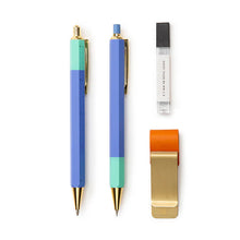 Load image into Gallery viewer, This image displays the open contents of the stationery set arranged neatly on a plain white background alongside a closed black notebook. The items include a teal multi-tool pen, a matching light blue mechanical pencil, a clear tube of lead refills, and a brass-colored metal page clip fitted with a bright orange elastic pen loop.
