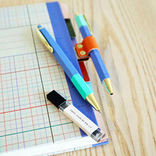 Load image into Gallery viewer, This image features a hexagonal multi-tool pen and a matching mechanical pencil, both sporting a color-blocked light blue and teal design finished with elegant gold metal tips and clips. Completing the collection is a small, clear container of 0.7 mm HB lead refills alongside a brushed-gold metal notebook clip with a bright orange loop to hold your writing instrument securely.
