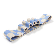 Load image into Gallery viewer, This image showcases the uncoiled elastic book band resting horizontally on a clean white surface, viewed from a slight side-angle. The durable fabric features a light blue and cream checkered pattern, with its top layer stitched down at intervals to form four wavy, standalone loops designed to hold writing utensils.
