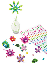 Load image into Gallery viewer, a clear glass vase holds a tall, handmade flower crafted from translucent lime green and sky blue pieces on a thin wire stem. Scattered around the base of the vase are several smaller, completed floral creations in vibrant shades of pink, orange, and teal, sitting alongside a large white sheet filled with neat rows of the colorful, translucent sticker dots used to make them.
