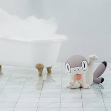 Load image into Gallery viewer, The grooming Sharkitty figurine sitting on a white marble tiled floor, its back leg raised with pink paw pads exposed and its tongue sticking out. In the background sits a white clawfoot bathtub overflowing with fluffy white bubble bath suds.
