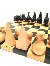Load image into Gallery viewer, A perspective view across the surface of a chessboard set up with geometric light and dark wooden pieces.
