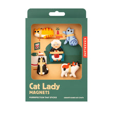 Load image into Gallery viewer, a deep green box with a large cutout window displaying a set of "Cat Lady Magnets" arranged like a tiny living room scene. Inside, five sculpted refrigerator magnets are visible, including a sweet grandmother figure sitting in an armchair surrounded by four playful cats: an orange tabby, blue striped tabby, black-and-white tuxedo, and calico patterns.
