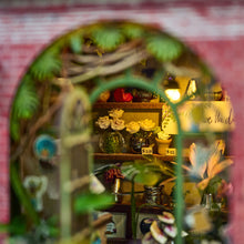 Load image into Gallery viewer, A warm, close-up shot framed through the arched doorway reveals tiny potted white roses on display shelves labeled with small price tags inside the shop.
