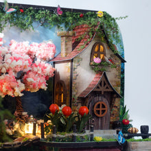 Load image into Gallery viewer, A detailed shot highlights a two-story miniature cottage with a lighted upper window, a pink cherry blossom tree, orange flower accents, and a blue butterfly perched near the wooden door.
