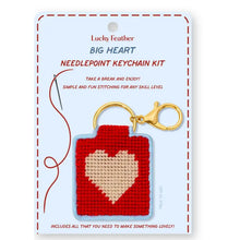 Load image into Gallery viewer, This image shows a needlepoint keychain kit packaged flat against a light blue card with a stitched red border. The card displays a pre-made sample featuring a red woven square with a beige heart in the center, attached to a gold key ring and clasp, alongside an illustration of a stitching needle.
