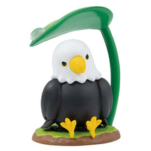 Load image into Gallery viewer, A small bald eagle figurine sitting on a grassy base against a plain white background, featuring a plump black body, bright yellow feet, and a classic white head with a sharp yellow beak. The eagle looks ahead under a curved green leaf stem that forms a protective umbrella over its head, complete with a clear raindrop on top.
