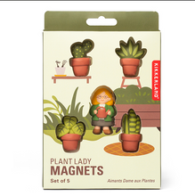 Load image into Gallery viewer, olive-green box with a large cutout window displaying a set of five "Plant Lady Magnets" arranged like a tiny garden scene. Inside, a central magnet of a smiling, glasses-wearing woman holding a watering can is surrounded by four distinct magnets of potted houseplants, including a cactus, a snake plant, and two leafy green varieties in terracotta-colored pots.
