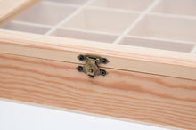 Load image into Gallery viewer, A close-up view showing the small antique brass latch on a light-colored wooden box with internal grid compartments visible beneath a glass top.
