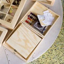 Load image into Gallery viewer, An overhead view showing several open light wood display boxes containing craft materials, paper swatches, scientific diagrams, and insect specimens.
