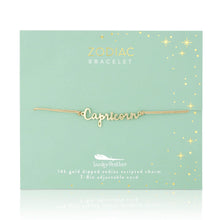 Load image into Gallery viewer, This image shows a gold "Capricorn" script bracelet mounted flat against a light, mint-green square card adorned with tiny metallic gold stars and dots. The dainty bracelet features a delicate cursive nameplate charm dipped in 14k gold, threaded onto a slim, adjustable tan cord.
