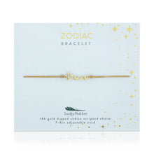 Load image into Gallery viewer, This image shows a gold "Pisces" script bracelet mounted flat against an exceptionally pale, icy-blue square card decorated with tiny metallic gold stars and dots. The minimalist bracelet features a delicate cursive nameplate charm dipped in 14k gold, threaded onto a thin, adjustable tan cord.
