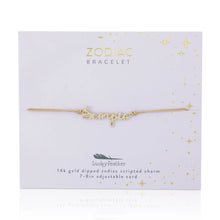 Load image into Gallery viewer, This image shows a gold "Scorpio" script bracelet mounted flat against a pale, soft lavender square card decorated with tiny metallic gold stars and dots. The minimalist bracelet features a delicate cursive nameplate charm dipped in 14k gold, threaded onto a thin, adjustable tan cord.
