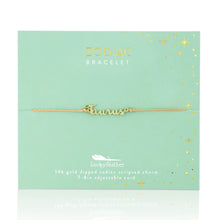 Load image into Gallery viewer, This image shows a gold "Taurus" script bracelet mounted flat against a light seafoam green square card adorned with tiny metallic gold stars and dots. The minimalist bracelet features a delicate cursive nameplate charm dipped in 14k gold, threaded onto a thin, adjustable tan cord.
