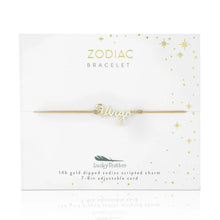 Load image into Gallery viewer, This image shows a gold "Virgo" script bracelet mounted flat against a clean white square card decorated with tiny metallic gold stars and dots. The minimalist bracelet features a delicate cursive nameplate charm dipped in 14k gold, threaded onto a thin, adjustable tan cord.
