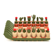Load image into Gallery viewer, A front-angle view of a mini chess set featuring dark green and light tan potted cactus pieces set up on a terracotta-and-cream checkered board.
