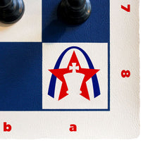 Load image into Gallery viewer, A close-up view of the corner square on a vinyl chess board showing a red and blue Gateway Arch and king chess piece logo alongside algebraic grid markers.
