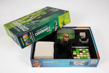 Load image into Gallery viewer, An open box of the board game Codenames Duet, shown with the green-toned top lid resting partially propped against the bottom tray on a white surface. Inside the black plastic insert are stored components, including stacks of white word cards, illustrated green agent tiles, and a grid keycard displaying a pattern of green four-pointed stars and dark beige squares.
