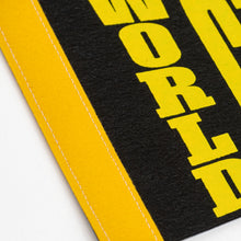 Load image into Gallery viewer, This close-up photo shows the left edge of the black felt pennant featuring a yellow strip bound with white stitching. Printed vertically in bold yellow letters on the felt surface is the word "WORLD."
