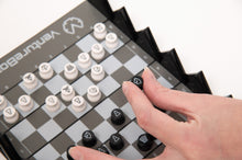 Load image into Gallery viewer, A close-up view of a hand placing a black knight piece onto the grid of a VentureBoard mini travel chess set during mid-game play.
