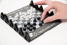 Load image into Gallery viewer, A hand adjusts a black piece on the compact grid of a fully set up VentureBoard mini travel chess set during play.
