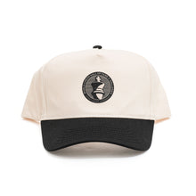 Load image into Gallery viewer, A two-tone baseball cap with an off-white crown and a contrasting black brim paired with a matching black top button. Centered on the front panel is a circular black patch featuring a white king chess piece icon encircled by the text "WORLD CHESS HALL OF FAME &amp; GALLERIES SAINT LOUIS, MISSOURI".
