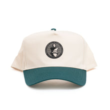 Load image into Gallery viewer, A two-tone baseball cap with an off-white crown and a contrasting green brim paired with a matching green top button. Centered on the front panel is a circular black patch featuring a white king chess piece icon encircled by the text "WORLD CHESS HALL OF FAME &amp; GALLERIES SAINT LOUIS, MISSOURI".
