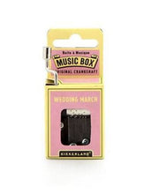Load image into Gallery viewer, This image shows the same small, hand-cranked music box packaging, this time featured in a light pink and pale yellow cardboard design. A silver metal crank extends up from the top left corner, and the front pink panel displays the text "WEDDING MARCH" directly above the cutout window revealing the internal metal mechanism.
