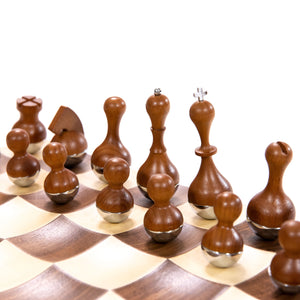 "Close-up of wobbling black chess pieces on a modern walnut and maple chessboard with chrome accents and a 3.5-inch king."